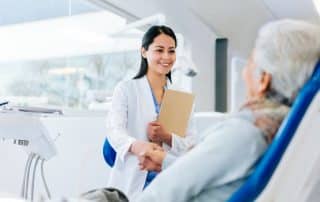 female dentist shaking hands with older woman in dentist chair