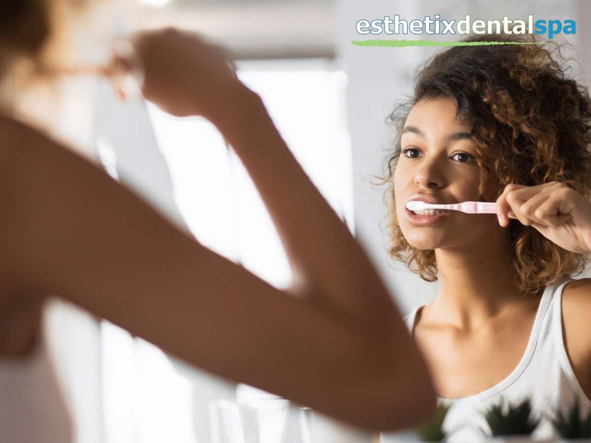 A smiling individual brushes their teeth, possibly managing tooth sensitivity