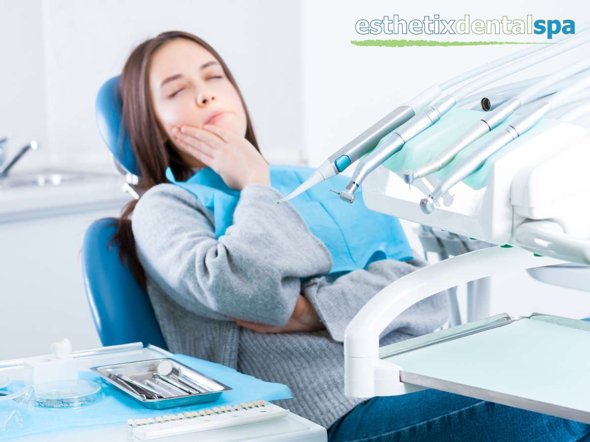 A patient holding her cheek in pain while sitting in a dental chair, possibly in need of endodontic therapy, with dental equipment in the foreground