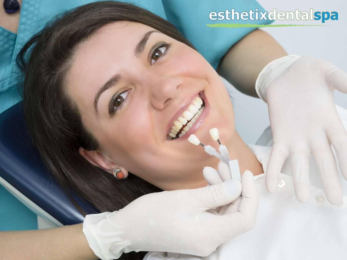 Dentist comparing shades for Porcelain Crowns vs. Composite Fillings with a smiling female patient